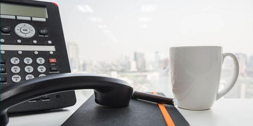 IP phone on office desk with notebook and coffee mug