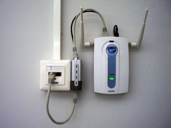 This Ethernet connection includes power over Ethernet (gray cable looping below), and a PoE splitter provides a separate data cable (gray, looping above) and power cable (black, also looping above) for a wireless access point. power over ethernet example